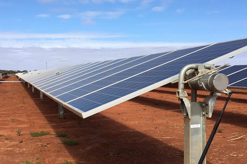 Long bank of chest high solar panels against blue sky on the red earth of the Sandfire copper mine near Meekatharra, WA