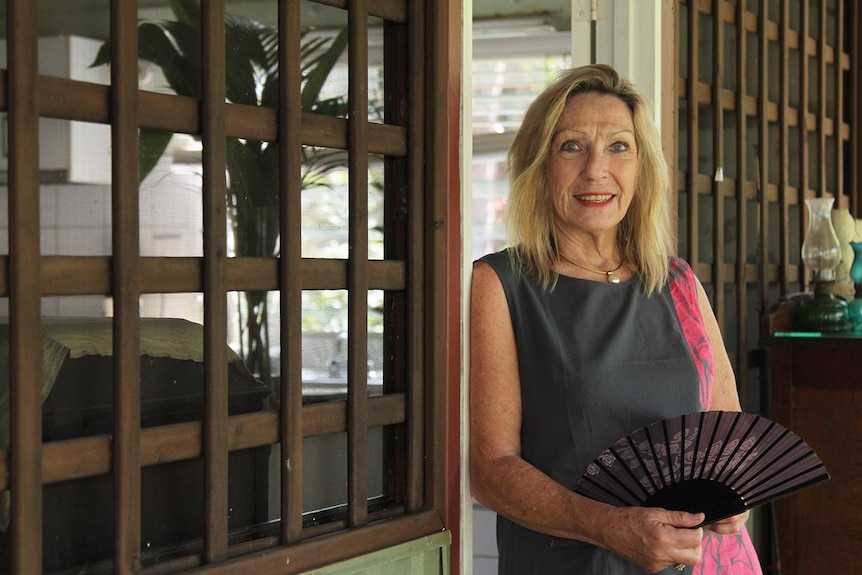 A photo of Judith Stevenson standing no the desk of her tropical home.