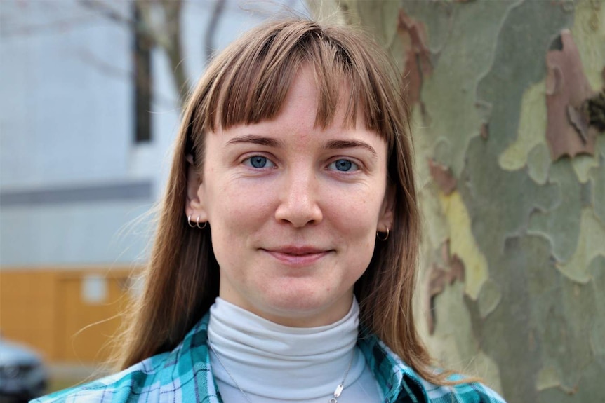 A close up of Aife wearing a white turtleneck jumper with a blue checked jacket.