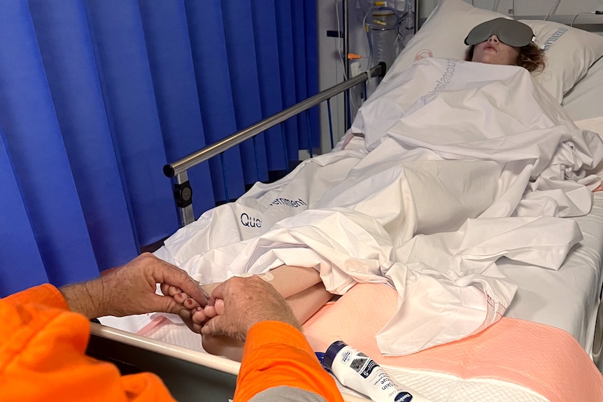 Man's hands rubbing the feet of his young adult daughter in a hospital bed