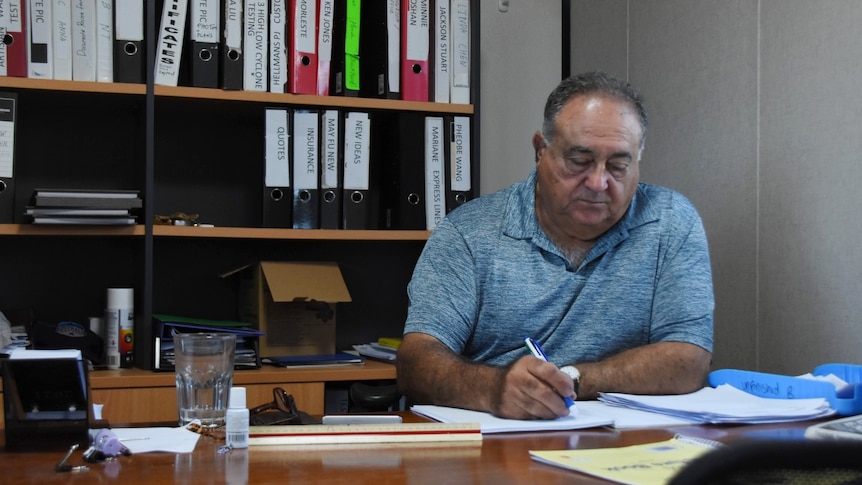 Builder George Milatos sits at his desk surrounded by folders and paperwork.