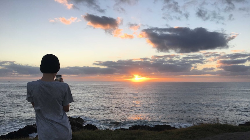 A boy taking a photo of a sunrise.