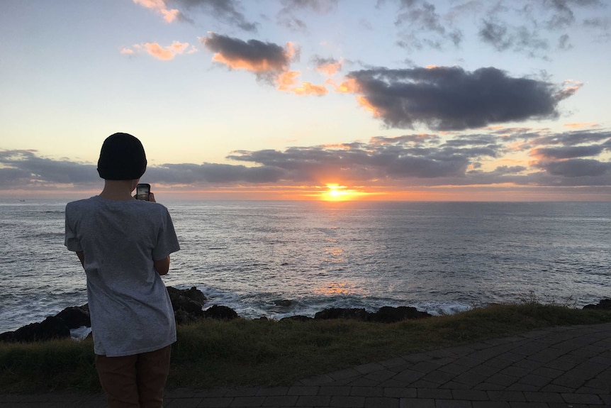 A boy taking a photo of a sunrise.