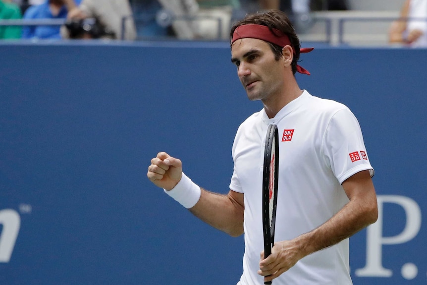 A male tennis player wearing a white shirt and red headband clenches his fist.