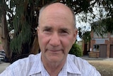 A man smiles into the camera as he sits in front of a tree