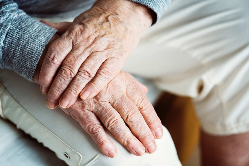 An elderly person's hands resting on knee in light coloured pants