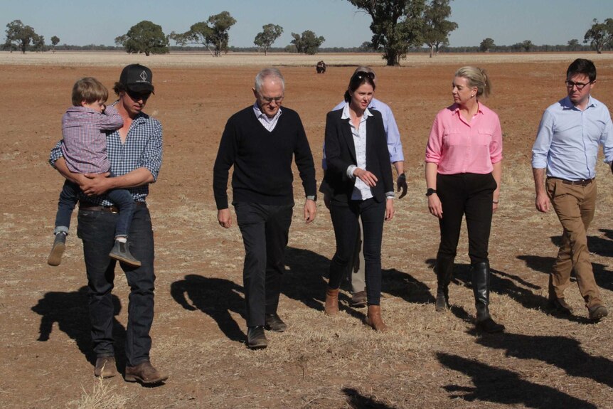 Malcolm Turnbull is recognisable among a group of people walking on dry land in Trangie. One man is carrying a toddler