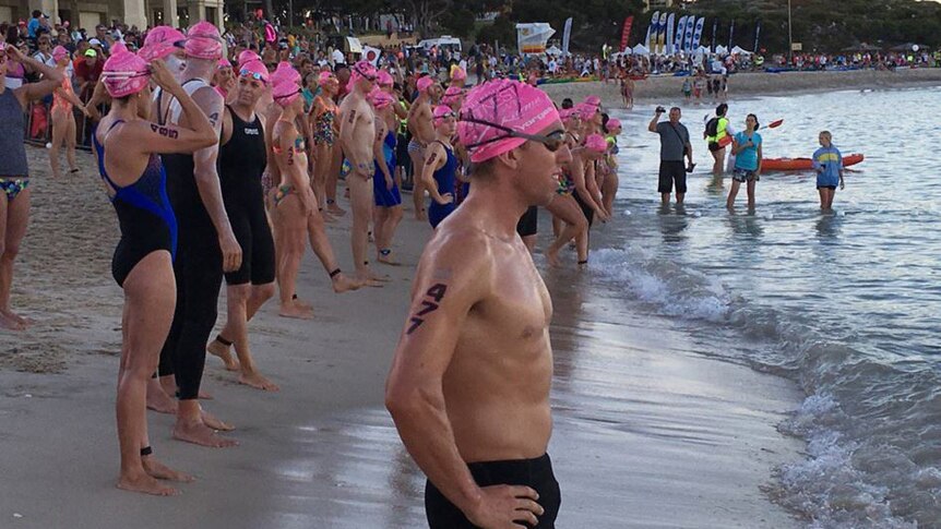 Swimmers in pink bathing caps along the shore at Cottesloe Beach.