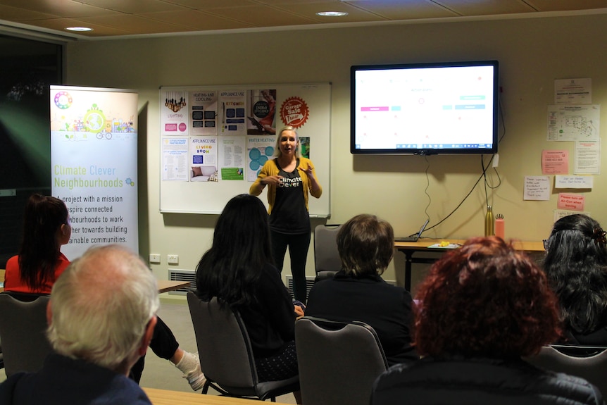 Woman stands in front of small crowd demonstrating an climate app on screen