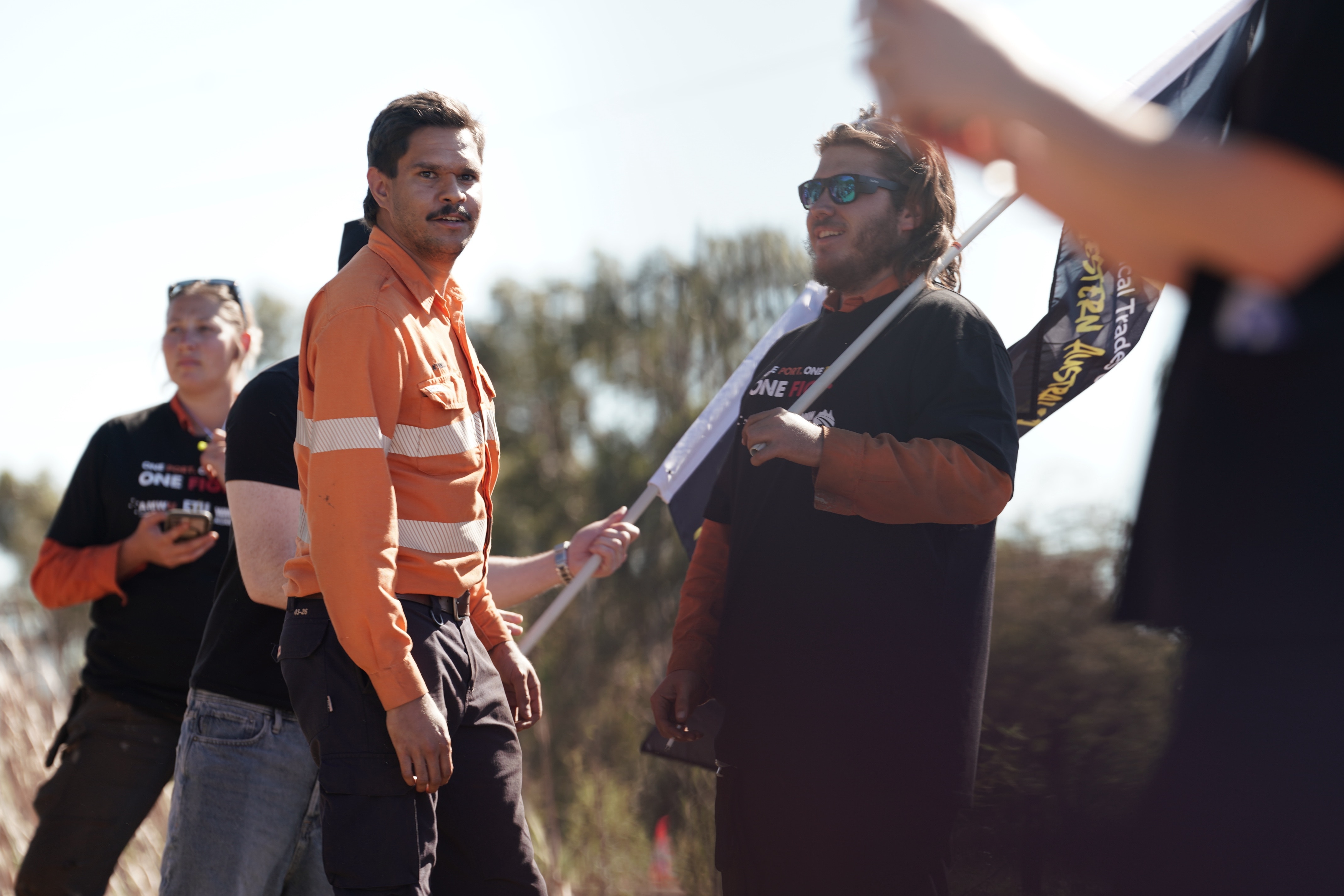A man in an orange unofrm stands in front of people holding flags.