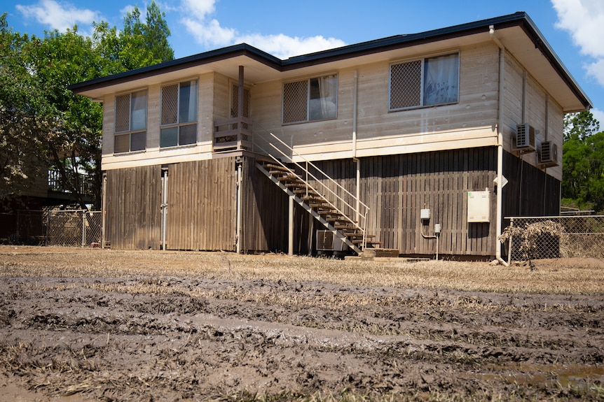 A Queenslander style house surrounded by muddy ground, has mud stains up to under the eves.