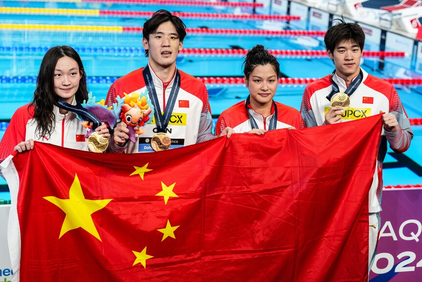 Chinese swimmers pose with the flag in front of a pool.