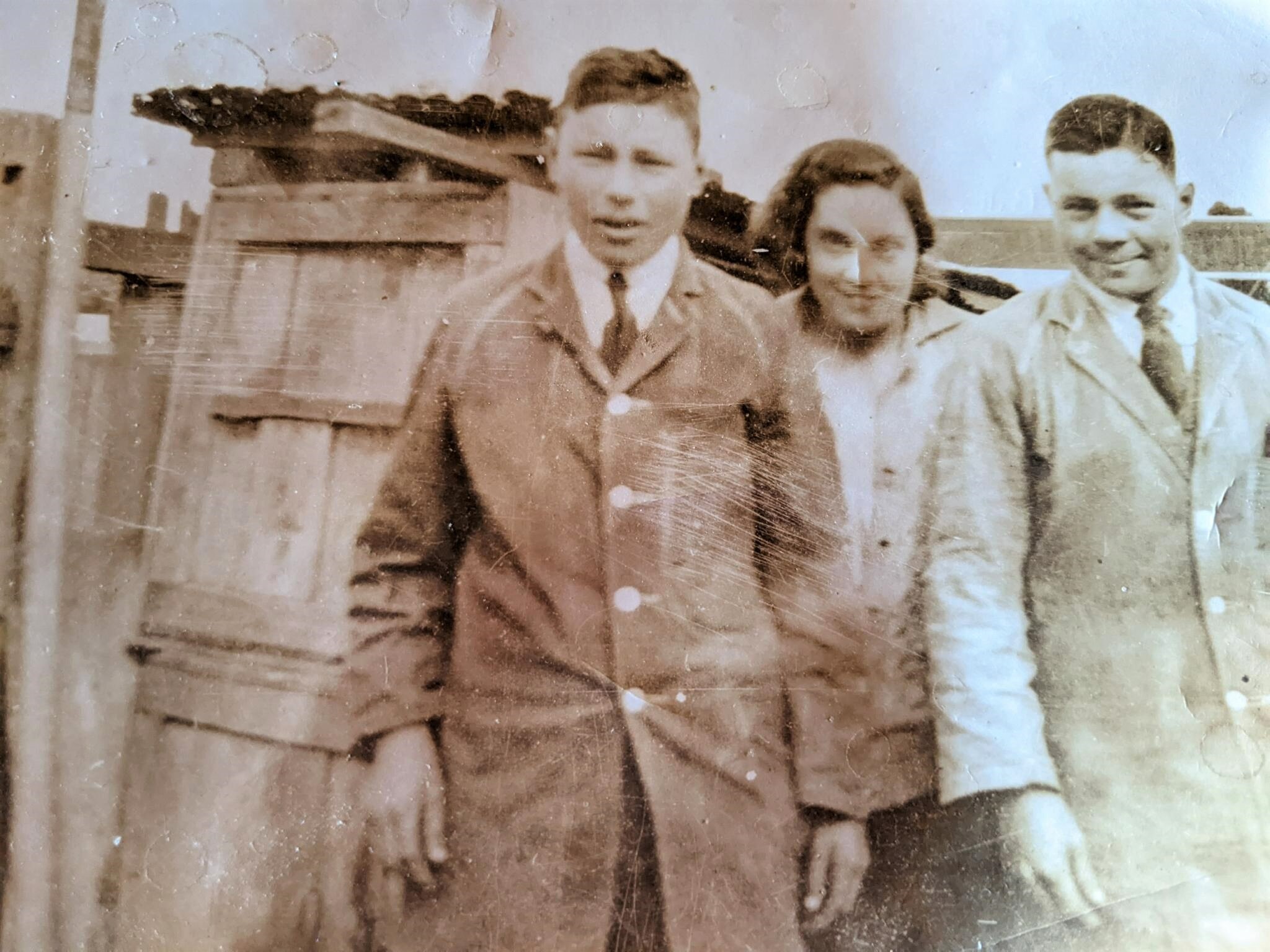An old discolored photo of a young man with a button down coat, his sister with dark shoulder length hair and another man.