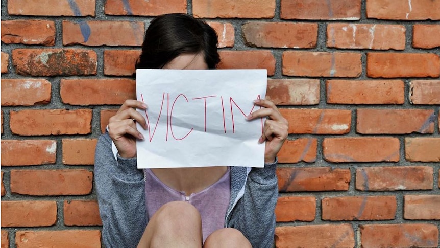 A woman holds up a 'Victim' sign.