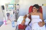 A woman in her thirties sits on a red chair hooked up to a dialysis machine