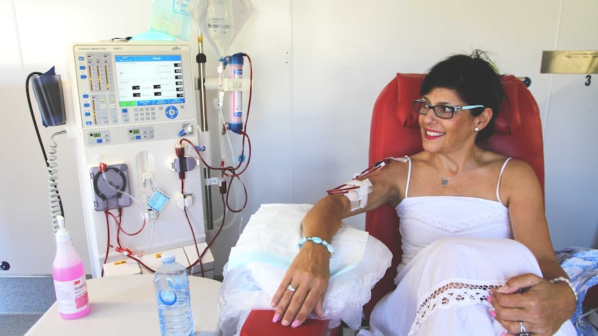 A woman in her thirties sits on a red chair hooked up to a dialysis machine