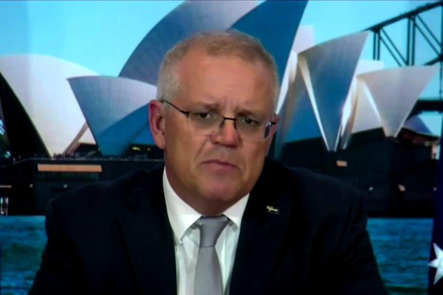 scott morrison in a suit with the australian flag and an image of the sydney opera house behind him