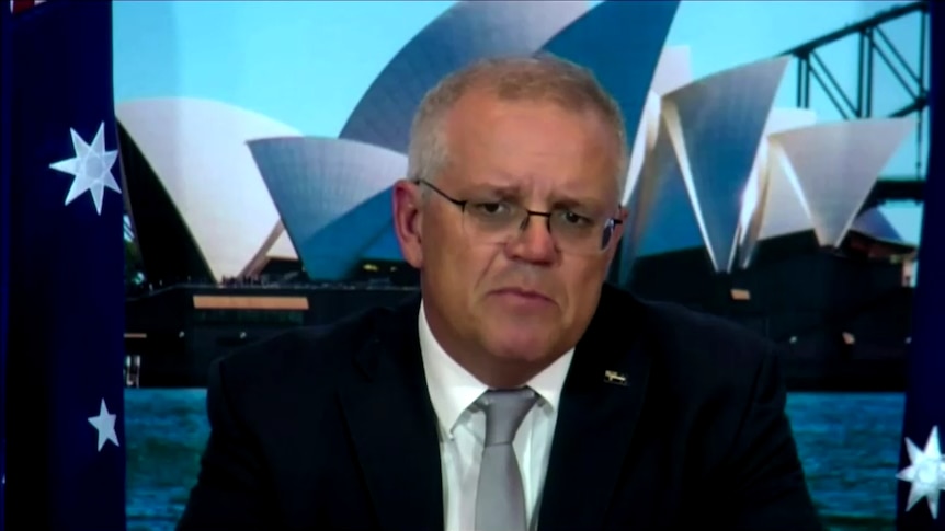 scott morrison in a suit with the australian flag and an image of the sydney opera house behind him