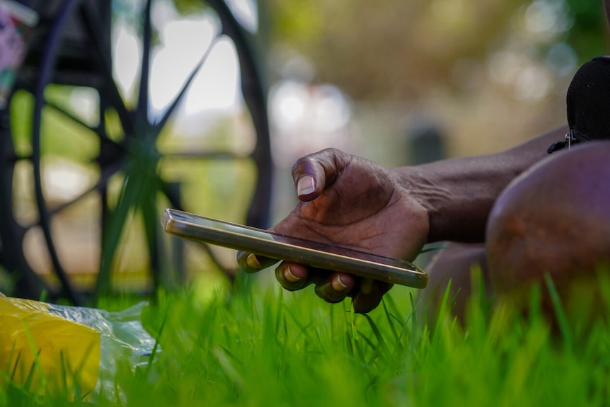 A person uses a phone while sitting on the grass
