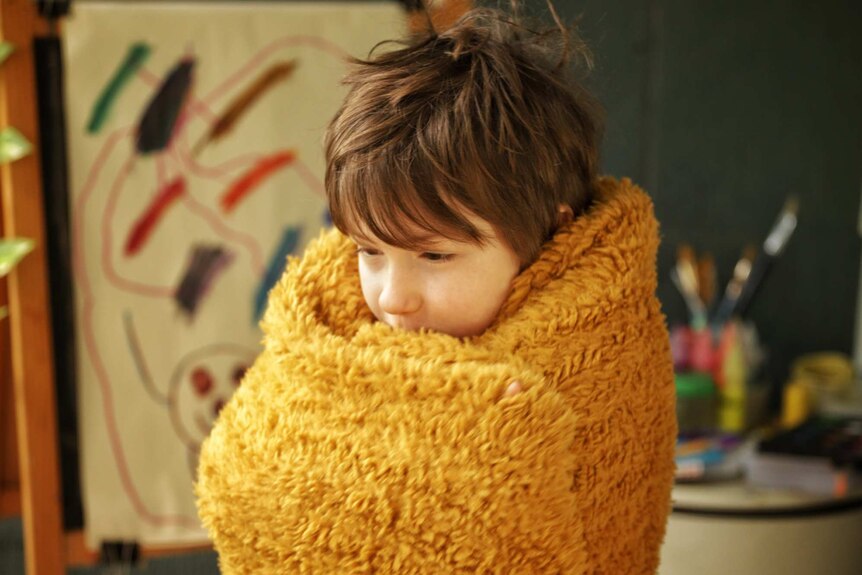 A child huddling wrapped in a blanket