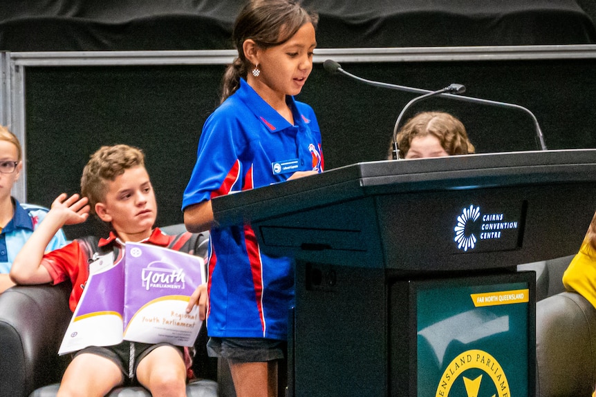 Kids wearing school uniform inside a convention centre at a mock-up parliament sitting.