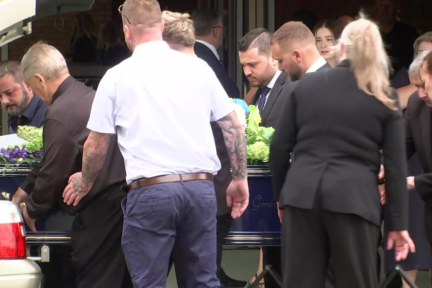 People loading a bllue casket into a hearse