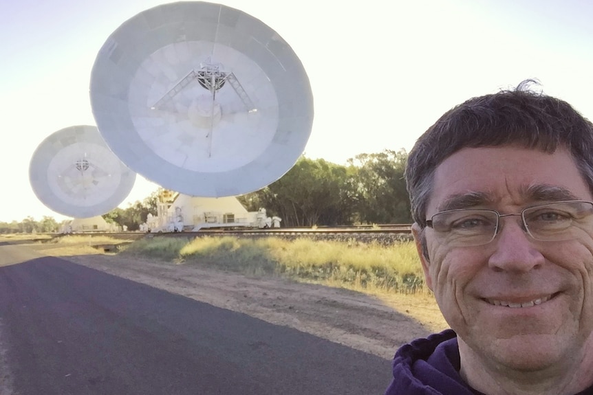 Matthew Bailes stands in front of two large satellite dishes.