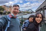 A young couple with chil on mother's back with Sydney harbour bridge in background.