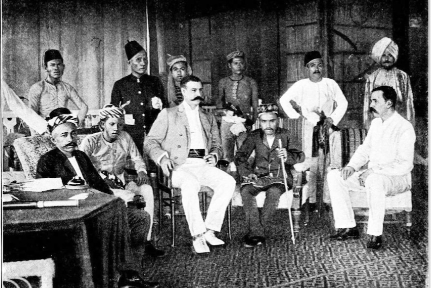 A black and white photo taken in 1899 of members of the BNBC sitting with the then Sultan of Sulu and his entourage.