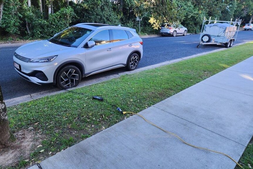 Extension cord running along pavement and grass charging an Electric vehicle