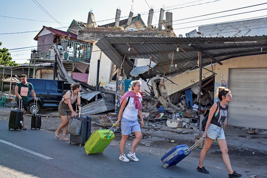 Foreign tourists pull their suitcases as they walk past damaged buildings in Pemenang, North Lombok.