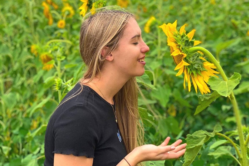 Jennifer Board smelling a sunflower in a field.
