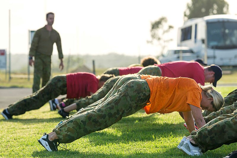 athletes and coaches perform planking exercises while a soldier watches on