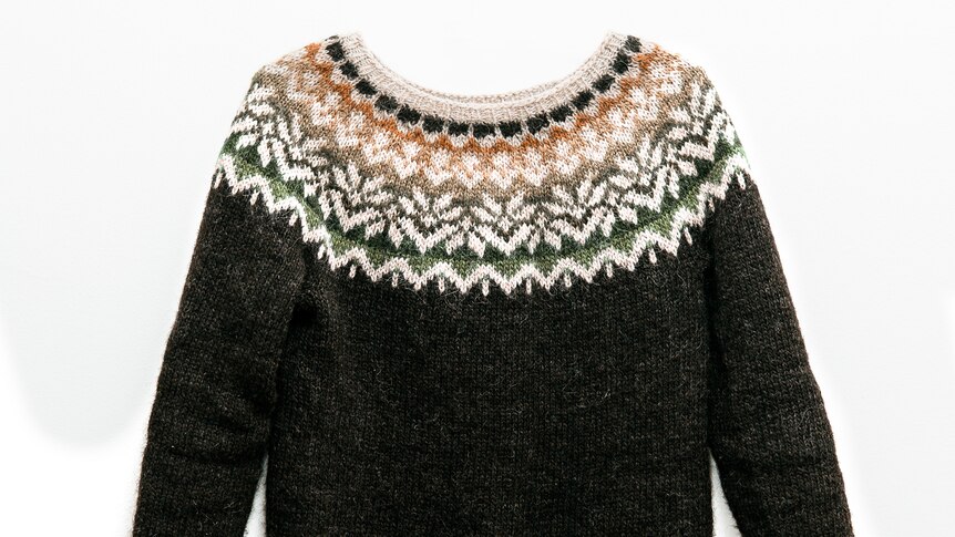 An icelandic sweater with brown whiet and orange patterns around the neck line