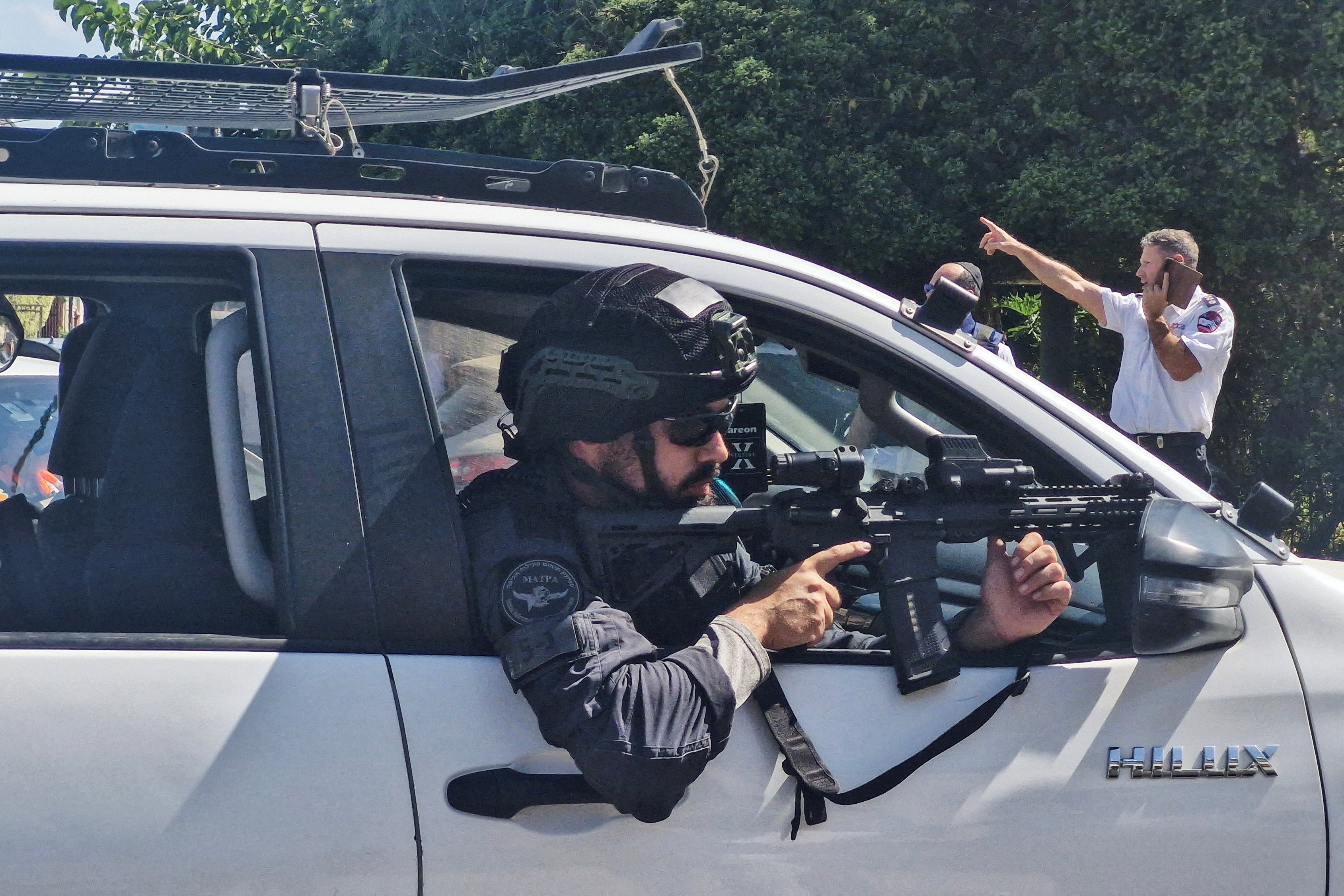 A man leans out of a car window while holding a long gun.