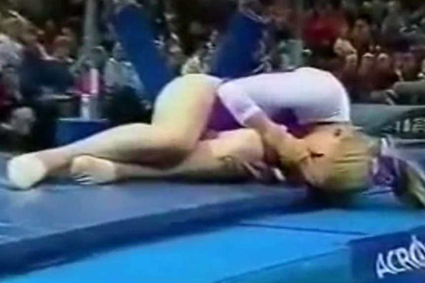 A young woman curled on a gymnastics mat hiding her face
