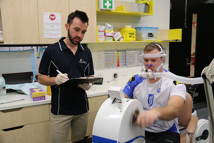 A man takes part in some testing using a breathing mask while another man takes observations