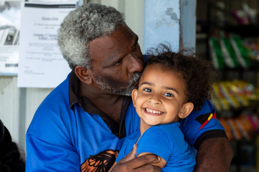 Young girl, smiling to camera, being held by her father.