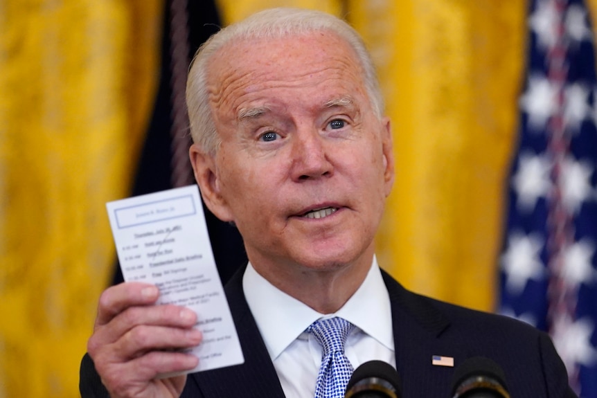 US President Joe Biden holds a note card that has the number of COVID-19-related American deaths as he speaks
