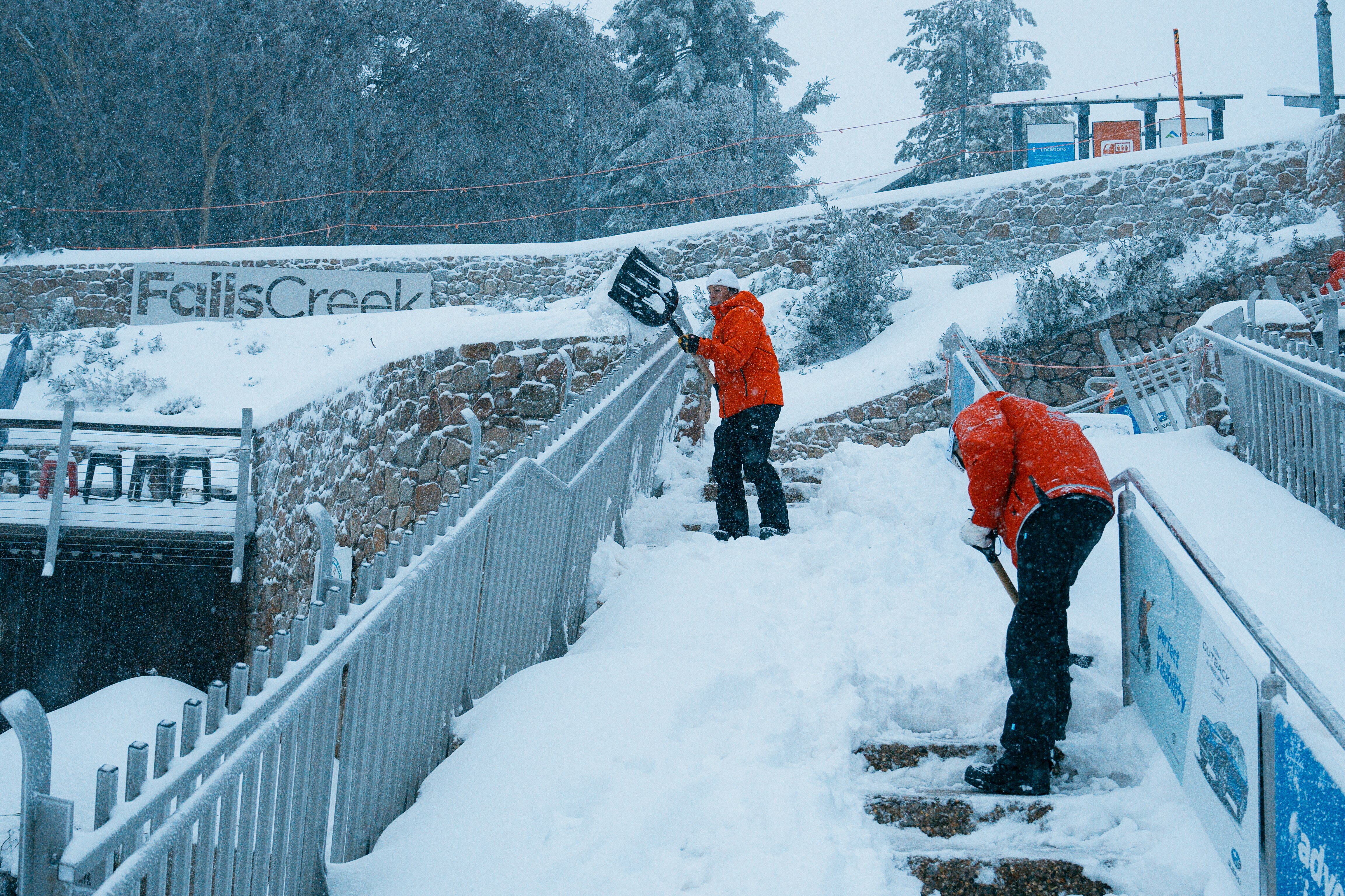 Dos personas que usan palas para eliminar la fuerte nieve de los escalones en Mountain Resort.