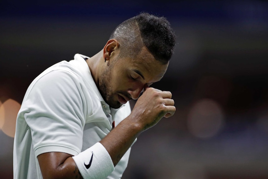 A tennis player stands with his head down and his fist in front of his face after losing a point.