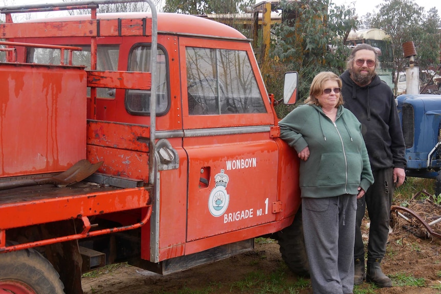 A man and woman lean against a vintage-red fire truck.