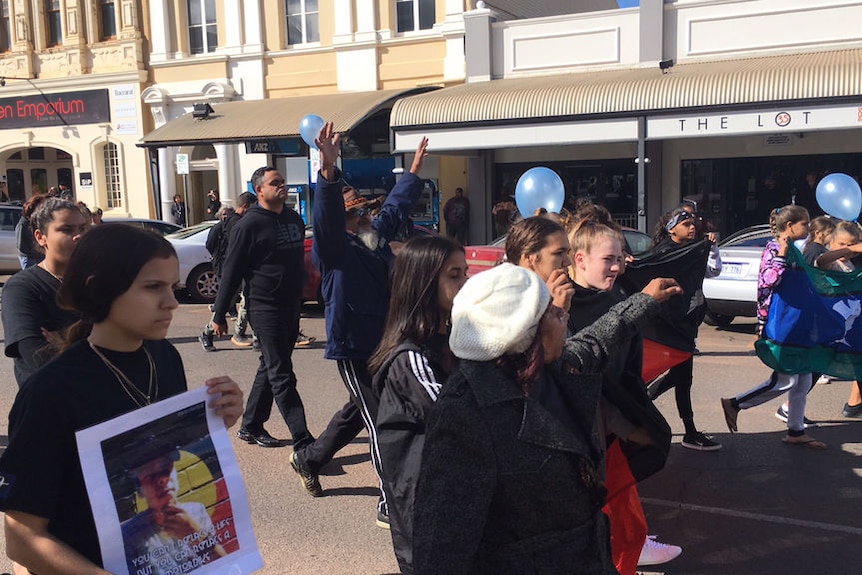 A crowd of protestors marches down Hannan Street in Kalgoorlie holding Indigenous flags.