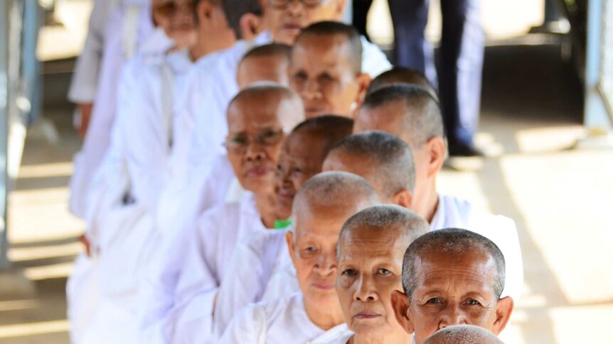 A group of elderly Cambodian nuns dressed in white stand in a line.