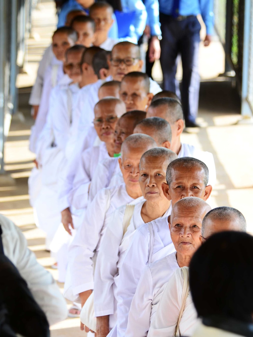 A group of elderly Cambodian nuns dressed in white stand in a line.