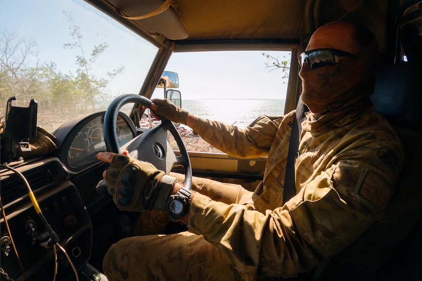 a man wearing khaki army uniform driving an army vehicle