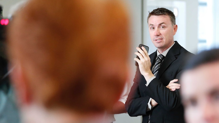 Ashby is holding his phone looking towards Hanson, whose heads is blurred in the foreground.