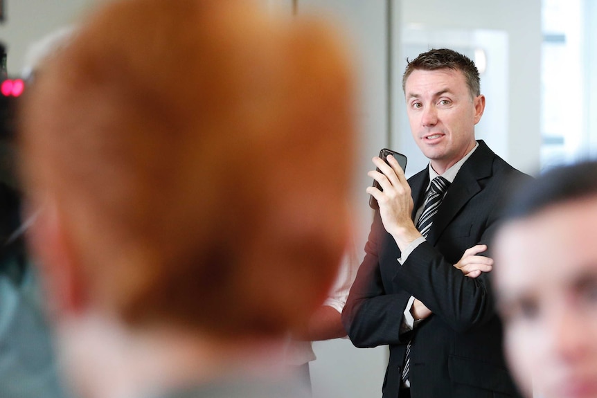 Ashby is holding his phone looking towards Hanson, whose heads is blurred in the foreground.