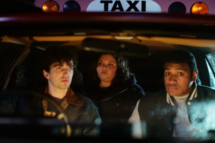 Two men and a woman sit inside a taxi.