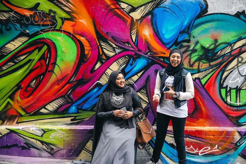 Kauthar and friend stand in front of graffiti wall.